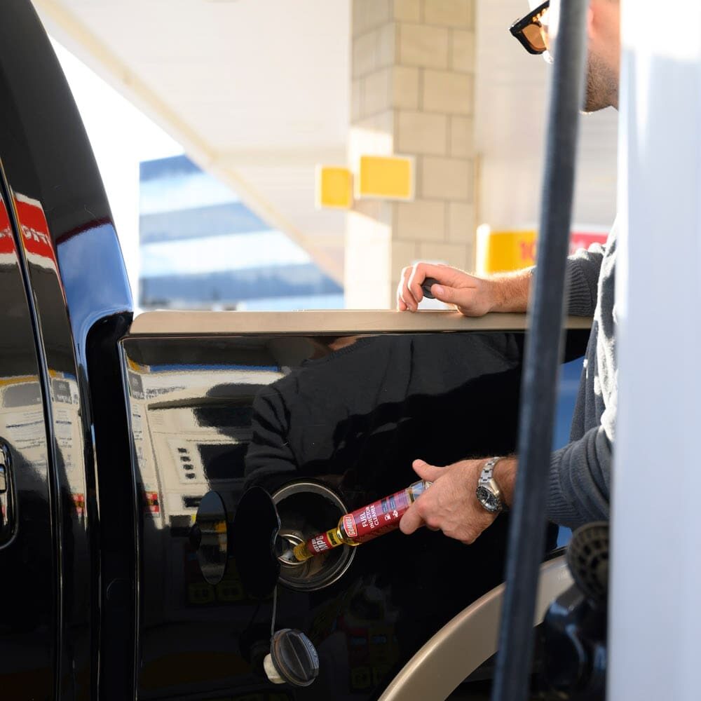 Person refueling a black pickup at a gas pump, with the nozzle in the fuel tank.